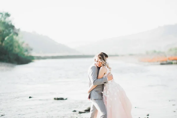 Elegante stijlvolle vrolijke blonde bruid en prachtige bruidegom op de achtergrond van een prachtige rivier in de bergen — Stockfoto