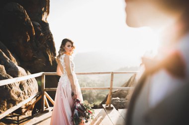 Yeni evli çift, gelin ve damat öpüşüyor, mükemmel dağ manzarasında sarılıyorlar, mavi gökyüzü