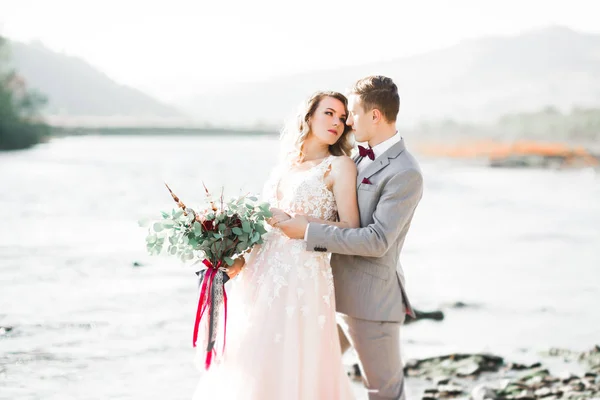 Elegante stilvolle glückliche blonde Braut und wunderschöner Bräutigam vor dem Hintergrund eines schönen Flusses in den Bergen — Stockfoto