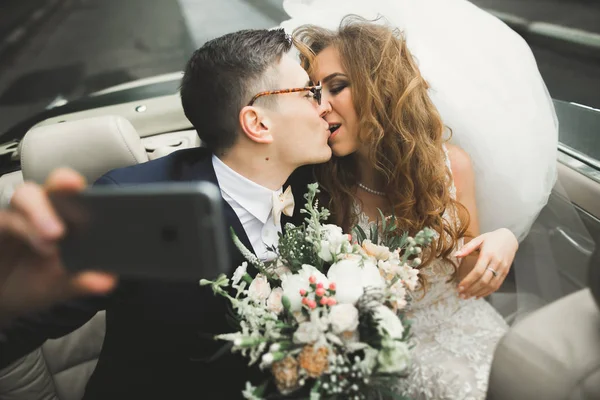 Happy bride and groom making selfie at their wedding in retro car — Stock Photo, Image