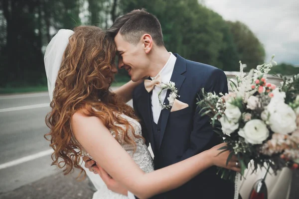 Стильная свадебная пара, невеста, жених целуется и обнимается на ретро-машине — стоковое фото