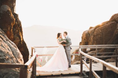 Yeni evli çift, gelin ve damat öpüşüyor, mükemmel dağ manzarasında sarılıyorlar, mavi gökyüzü