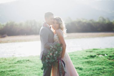 Güzel düğün çifti bir dağ nehrinin kıyısında taşlarla öpüşüp kucaklaşıyorlar.