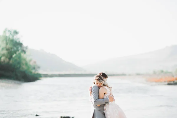 Elegante noiva loira feliz e lindo noivo no fundo de um belo rio nas montanhas — Fotografia de Stock