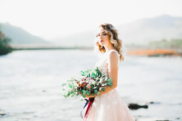 Portrait of stunning bride with long hair posing with great bouquet near river — Stock Photo, Image