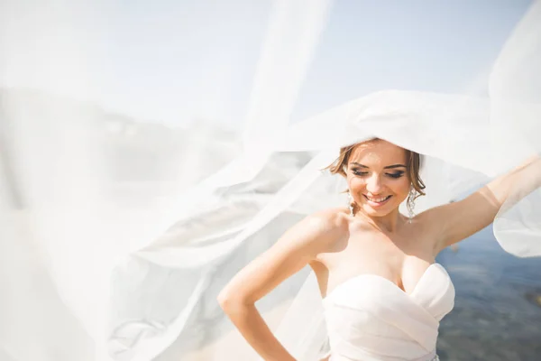 Preciosa novia en vestido de novia blanco posando cerca del mar con hermoso fondo —  Fotos de Stock