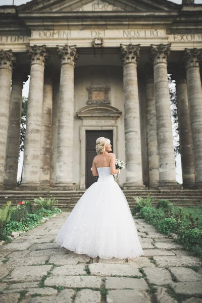 Bella sposa elegante con abito da sposa perfetto e bouquet in posa vicino al vecchio castello — Foto Stock