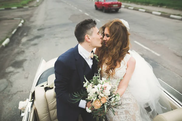 Stilvolles Hochzeitspaar, Braut, Bräutigam küssen und umarmen sich im Retro-Auto — Stockfoto