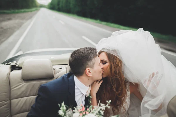 Стильная свадебная пара, невеста, жених целуется и обнимается на ретро-машине — стоковое фото