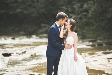 Şık şık mutlu esmer gelin ve dağlarda güzel bir nehir arka plan üzerinde muhteşem damat