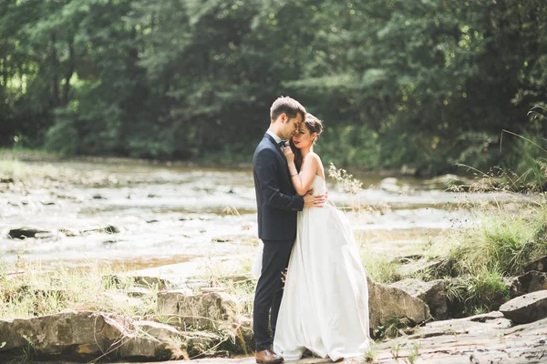 Elegante gentile sposo elegante e sposa vicino al fiume con pietre. Matrimonio coppia innamorata — Foto Stock