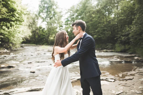 Elegante noivo elegante doce e noiva perto do rio com pedras. Casamento casal apaixonado — Fotografia de Stock