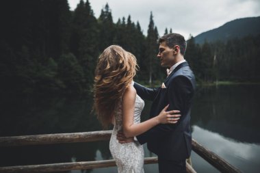 Yeni evli çift, gelin ve damat öpüşüyor, mükemmel dağ manzarasında sarılıyorlar, mavi gökyüzü