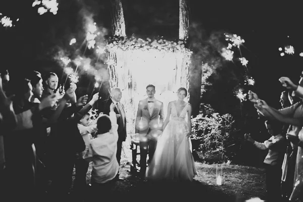 Goedenavond huwelijksceremonie. De bruid en bruidegom hand in hand op een achtergrond van lichten en lantaarns. — Stockfoto
