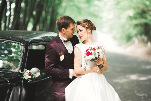 Feliz casal recém-casado, homem e mulher beijando perto de carro retro elegante — Fotografia de Stock