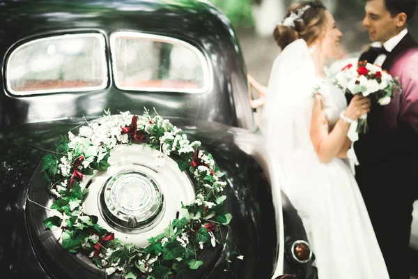 Feliz casal recém-casado, homem e mulher beijando perto de carro retro elegante — Fotografia de Stock