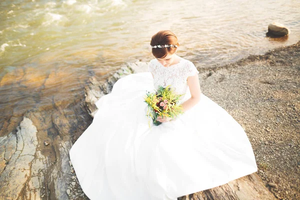 Splendida bella sposa sorride mentre posa sul fiume con bouquet — Foto Stock