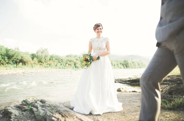 Nevěsta a ženich drží krásné svatební kytice. Pózování v blízkosti řeky — Stock fotografie
