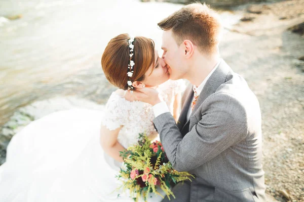 Elegante novio elegante y elegante novia cerca del río con piedras. Pareja de boda enamorada — Foto de Stock