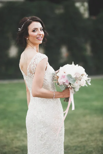 Bella sposa in elegante vestito bianco che tiene bouquet in posa nel parco — Foto Stock