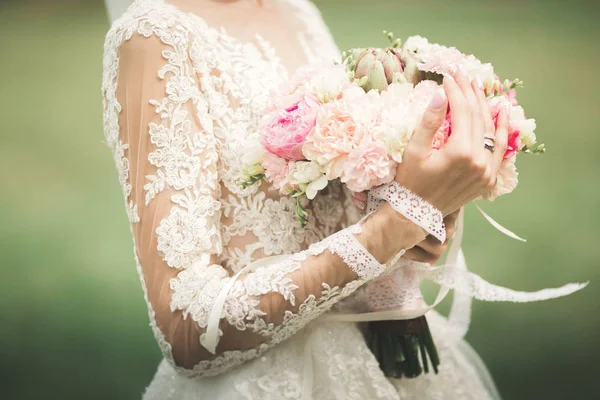 Красивая невеста в элегантном белом платье держа букет позируя в парке — стоковое фото