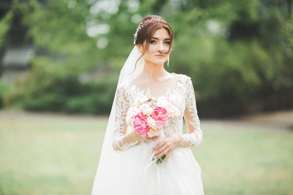 Cantik pengantin dalam gaun putih elegan memegang karangan bunga berpose di taman — Stok Foto