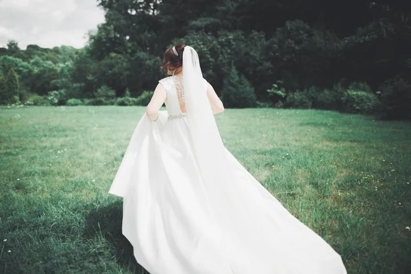 Mooie brunette bruid in elegante witte jurk met boeket poseren nette bomen — Stockfoto