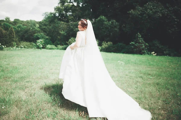 Mooie brunette bruid in elegante witte jurk met boeket poseren nette bomen — Stockfoto