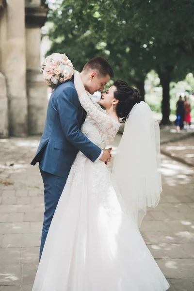 Ravissant couple de mariage heureux, mariée avec longue robe blanche posant dans la belle ville — Photo