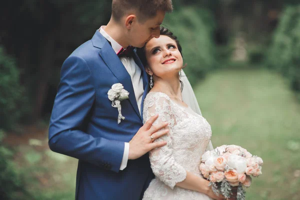 Snygga par glada nygifta promenader i parken på sin bröllopsdag med bukett — Stockfoto