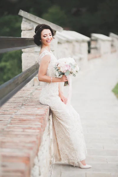 Bela noiva em elegante vestido branco segurando buquê posando no parque — Fotografia de Stock