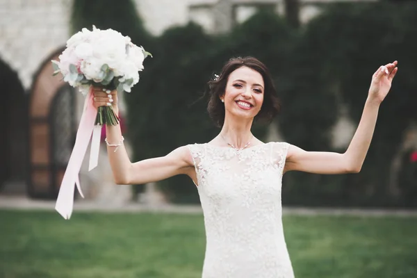 Gyönyörű menyasszony elegáns fehér ruha gazdaság csokor pózol a parkban — Stock Fotó