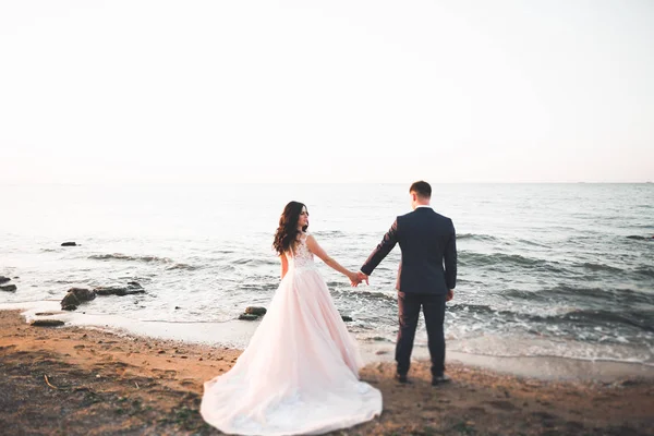 Свадебная пара целуется и обнимается на скалах у синего моря — стоковое фото