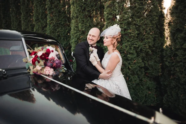 Heureux couple nouvellement marié, homme et femme embrasser près de voiture rétro élégant — Photo