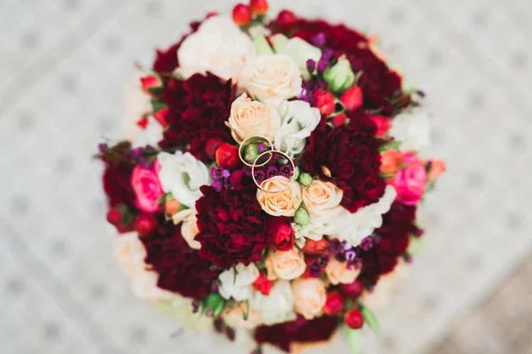 Gyönyörű tónusú kép jegygyűrűkkel a háttérben egy csokor virág — Stock Fotó