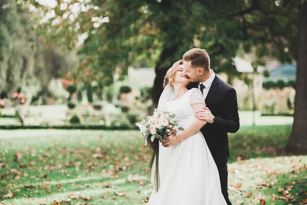 Casal elegante de recém-casados felizes andando no parque em seu dia de casamento com buquê — Fotografia de Stock