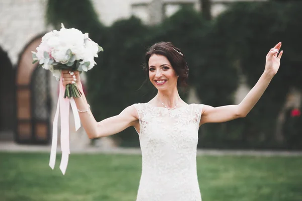Bella sposa bruna in elegante vestito bianco che tiene bouquet in posa alberi ordinati — Foto Stock