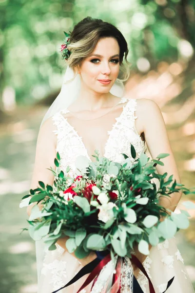 Belle mariée en élégante robe blanche tenant bouquet posant dans le parc — Photo