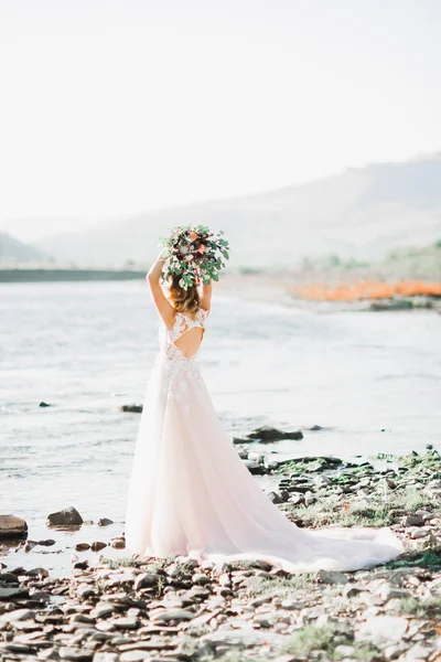 Ritratto di splendida sposa con capelli lunghi in posa con grande bouquet vicino al fiume — Foto Stock