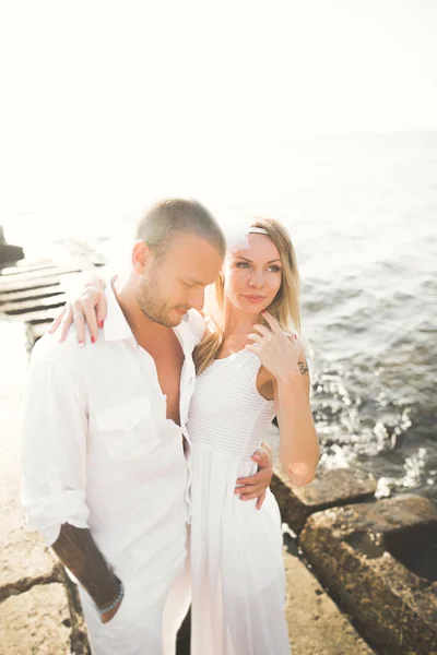 Romantica coppia amorevole posa su pietre vicino al mare, cielo blu — Foto Stock