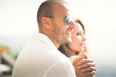 Düğün çifti mavi denizin yanındaki kayalarda öpüşüyor ve sarılıyor.