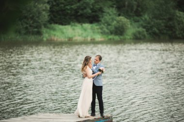 Zarif güzel düğün çifti bir göl kenarında günbatımında poz