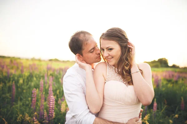 Noiva e noivo, levantando-se ao pôr do sol em um belo campo com flores, casal romântico — Fotografia de Stock