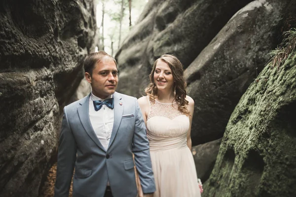 Hermosa pareja de boda besándose y abrazándose en el bosque con grandes rocas —  Fotos de Stock