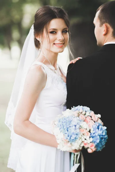 Casal elegante de recém-casados felizes andando no parque em seu dia de casamento com buquê — Fotografia de Stock