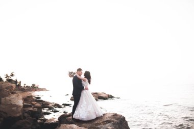 Düğün çifti, damat, gelin deniz kenarında ve mavi gökyüzünde poz veriyor.