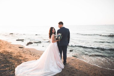 Düğün çifti, damat, gelin deniz kenarında ve mavi gökyüzünde poz veriyor.