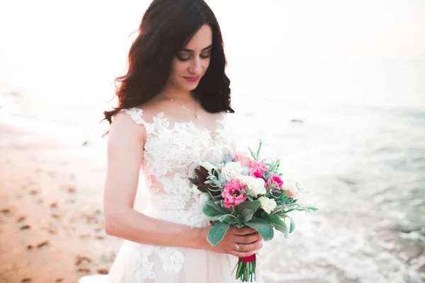 Hübsche Dame, Braut posiert in einem Brautkleid am Meer bei Sonnenuntergang — Stockfoto