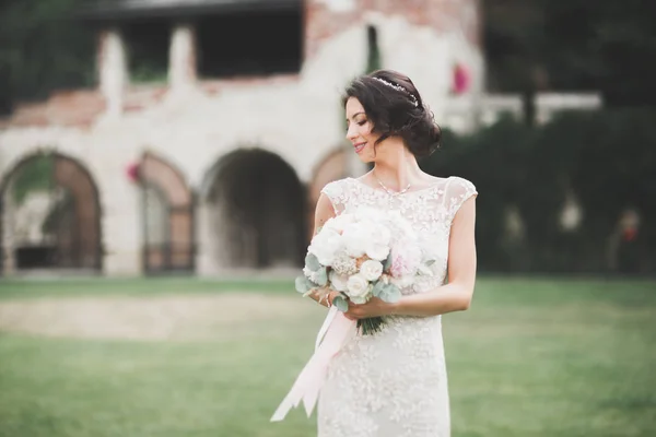 Mooie brunette bruid in elegante witte jurk met boeket poseren nette bomen — Stockfoto