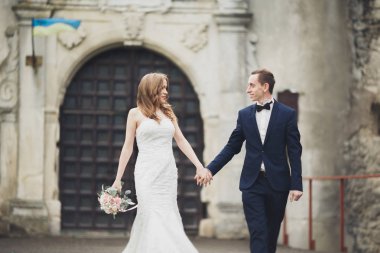 Güzel, romantik bir düğün. Yeni evliler. Eski kalenin yakınlarında sarılıyorlar.